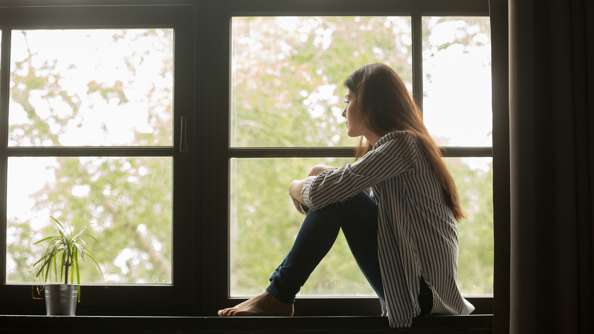 Thoughtful girl sitting on window seat looking out window