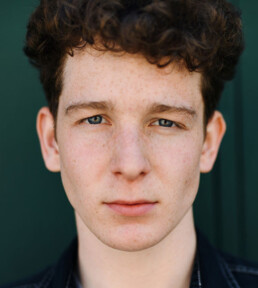 Serious young adult man looking at camera in front of green wall